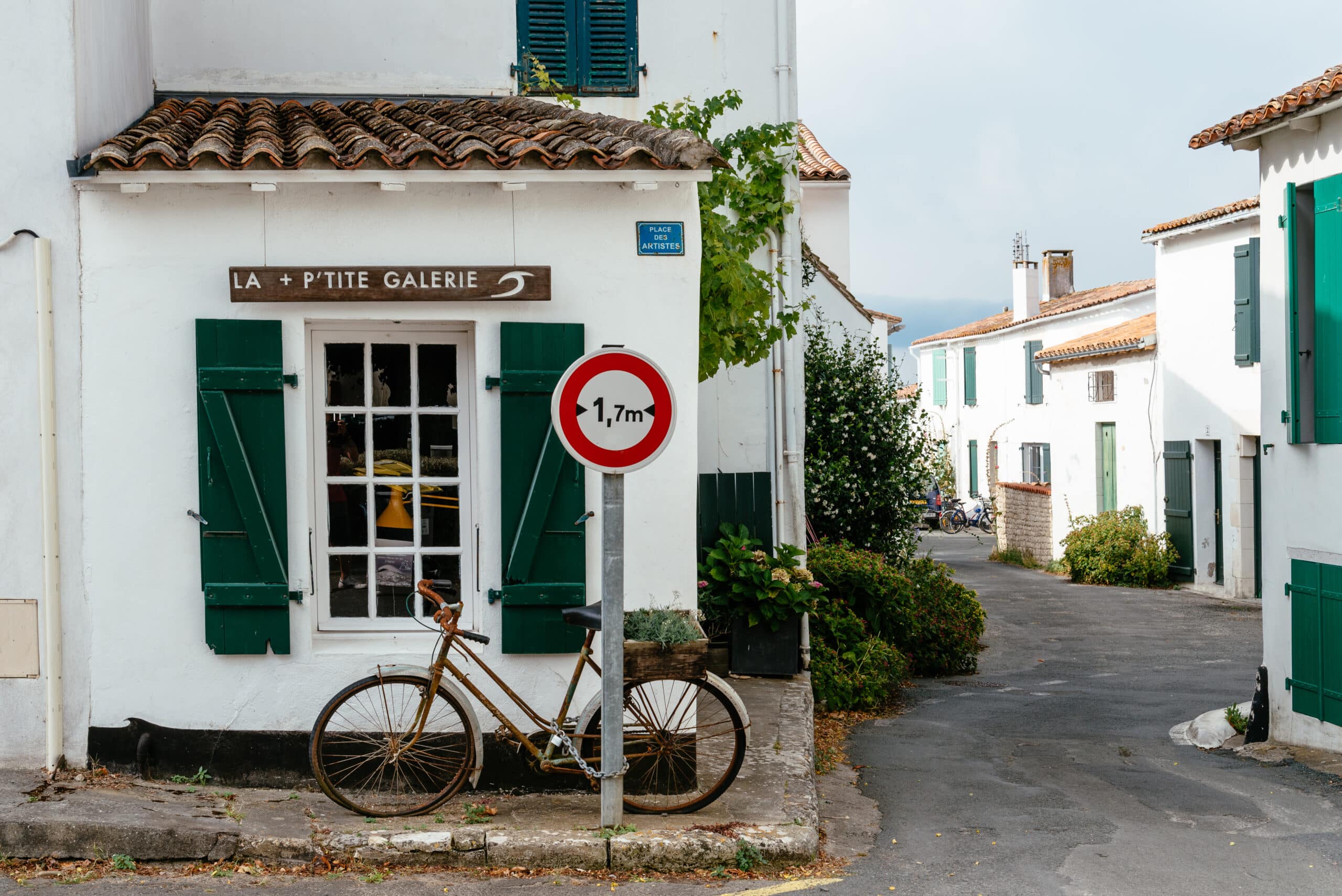 Maison blanche avec vélo, panneau et volets verts.