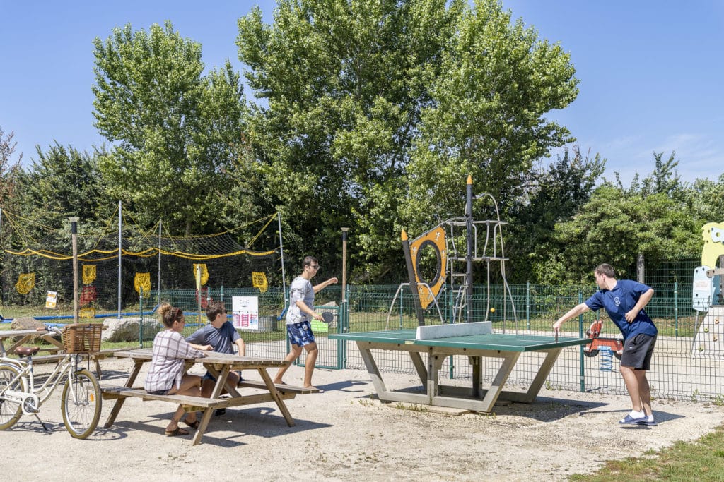 Personnes jouant au ping-pong en extérieur.