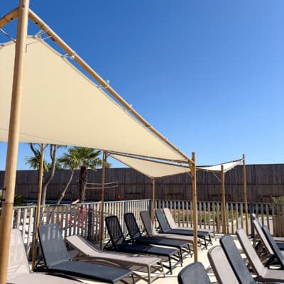 Terrasse ensoleillée avec chaises longues et pare-soleil.
