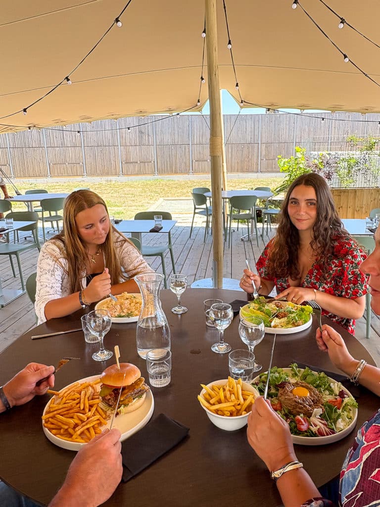 Personnes dînant en terrasse avec des plats variés.