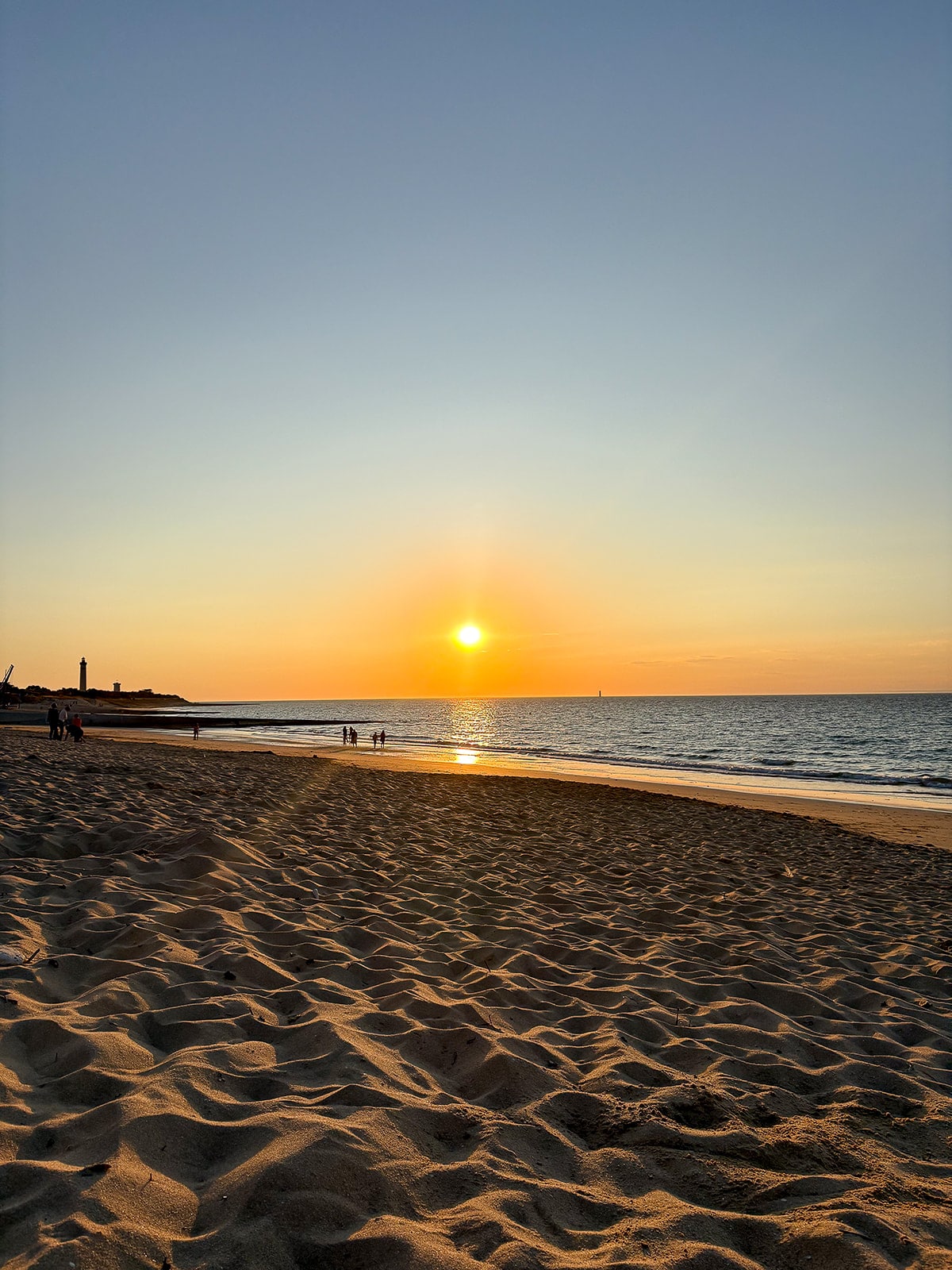 Coucher de soleil sur plage de sable, mer paisible.