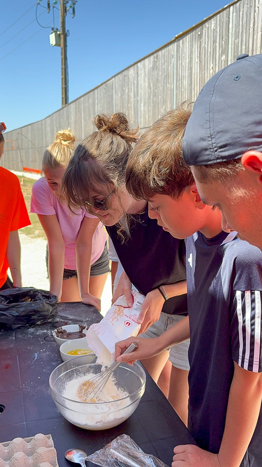 Groupe de jeunes cuisinant à l'extérieur, mélangeant des ingrédients.